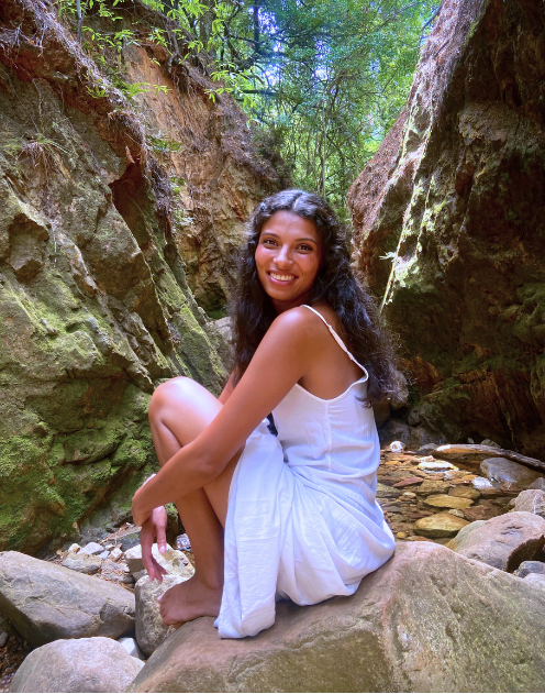 Donaë seated among mossy rocks in nature